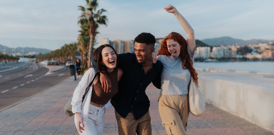 three young people dancing along the sidewalk near a beach
