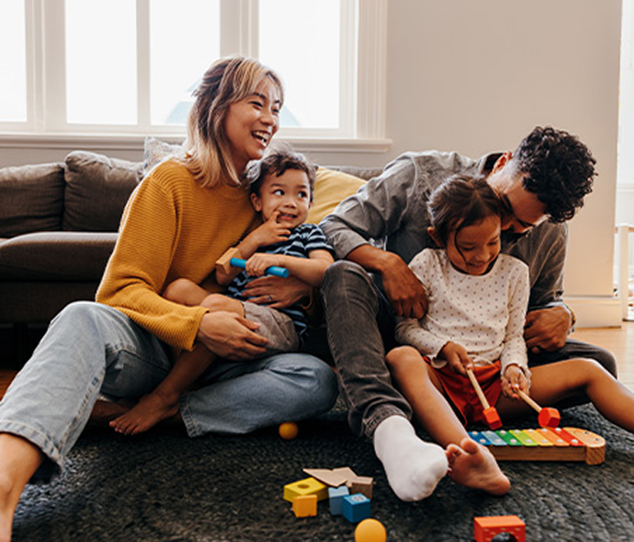 a family of 4 sitting in their living room, parents playing with kids