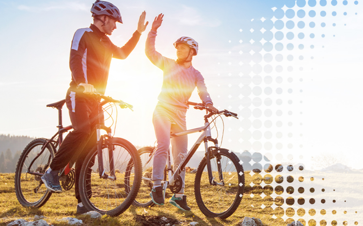 two bicyclists outside on a hill, high fiving each other