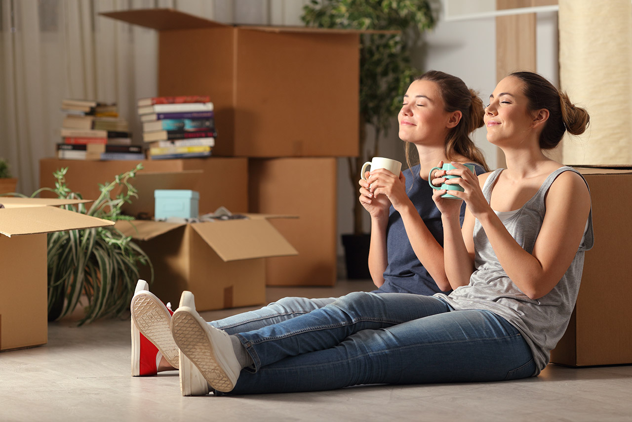 2 women enjoying tea while unpacking moving boxes